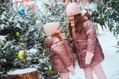Yılbaşı tatili için dekore edilmiş kışın karlı şehirde oynayan iki mutlu kız kardeşin Noel portresi. Çocuklar Noel tatillerini dışarıda geçirir ve seyahat ederler.