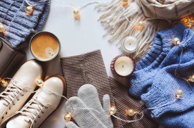 Modern kış ya da sonbahar kadın kıyafetleri üst manzarayı oluşturur. Noel ışıkları ve sonbahar yapraklarıyla bej ve mavi tonlarda şık ayakkabılar, süveterler ve aksesuarlar..