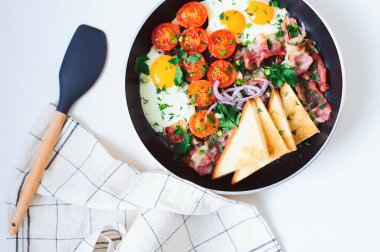 Çiftçilik tarzında lezzetli bir kahvaltı iki kişilik tabakta sunuluyor. Yağda yumurta, kiraz domatesleri, pastırma, kırmızı soğan ve kızarmış ekmek..