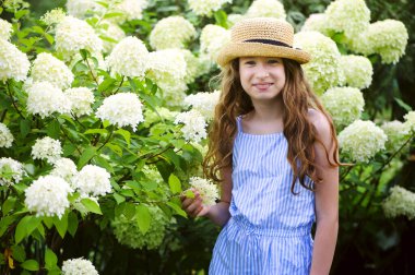 Mutlu çocuk yaz bahçesinde yürüyor, beyaz ortanca çalılarının yanında poz veriyor.
