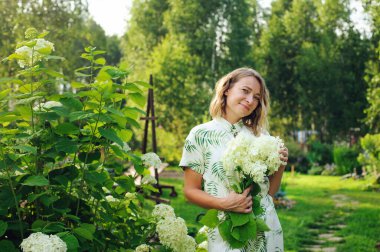 Güzel, genç bir bahçıvan yaz bahçesinde ortanca çiçekleriyle poz veriyor.