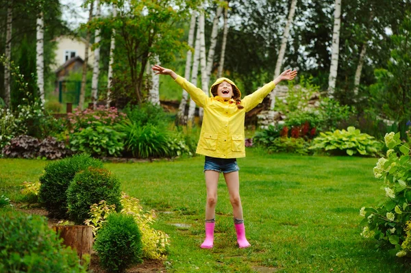穿着黄色雨衣的快乐小女孩在下雨天的夏日花园玩耍和玩乐 — 图库照片