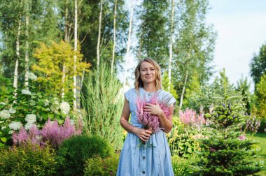Bahçıvan kadın özel bahçede bir buket astilbe çiçeğiyle poz veriyor. Kır yaşamı ve peyzaj tasarımı kavramı