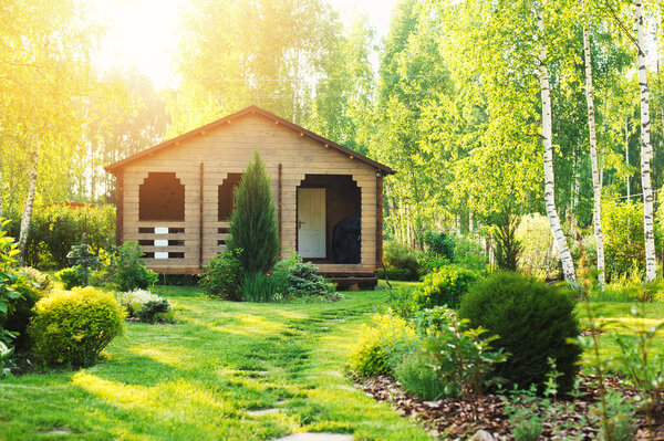 small wooden country house view in summer. Stone pathway, green lawn, conifers and shrubs. Garden design in english style.