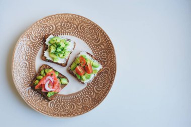 Tabakta servis edilen çeşitli tostlar, somon, avokado, krem peynir, salatalık ve kırmızı soğanlı sağlıklı kahvaltı.