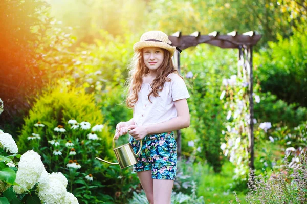 快乐的小女孩在夏天的花园里浇花 免版税图库图片