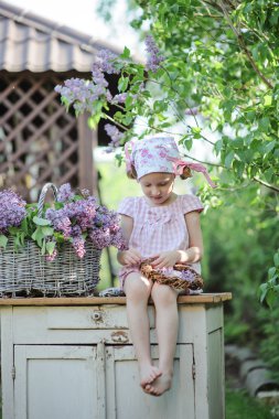 Şirin mutlu çocuk kız pembe kareli elbisesi ve Lila çelenk bahar bahçe içinde yapma çiçek kafa bandı