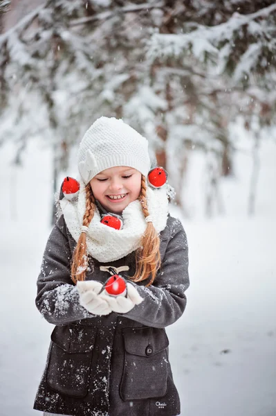 Linda niña en abrigo gris y sombrero blanco, bufanda y guantes juega con el toro de juguete en el bosque nevado de invierno — Foto de Stock