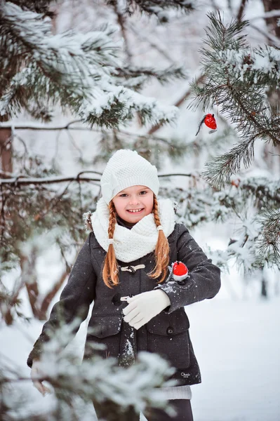 Schattig kind meisje in grijze vacht en witte hoed, sjaal en handschoenen speelt met speelgoed Goudvink in winter besneeuwde bos — Stockfoto
