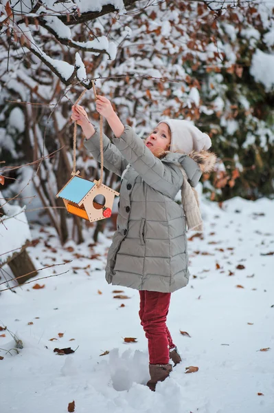 Mädchen hängt Vogelfutterhäuschen im schneebedeckten Wintergarten an Baum — Stockfoto