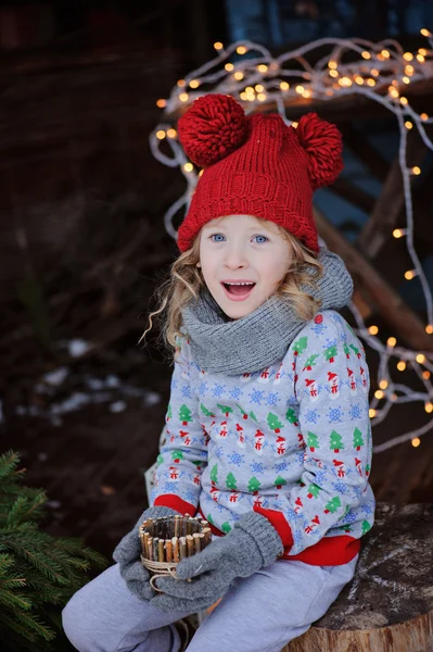 Ragazza carina in maglione di Natale e cappello rosso con portacandele in legno e rami di abete — Foto Stock