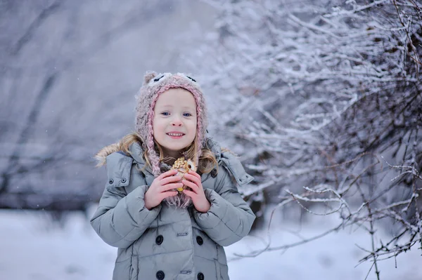 Cute happy child girl in owl hat and grey coat walking in snowy winter park — Stock Photo, Image