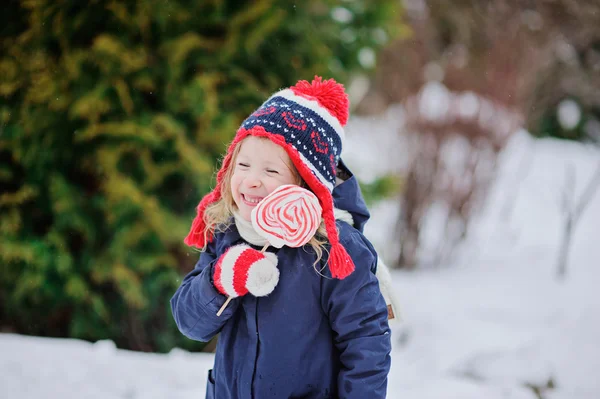 Ragazza carina che cammina nel giardino innevato invernale con caramelle natalizie — Foto Stock