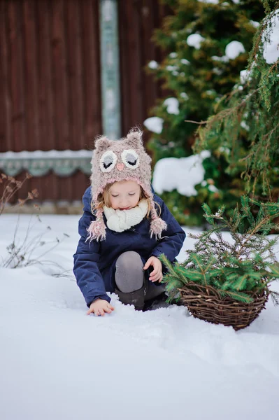 Cute happy child girl in owl hat and blue coat walking in winter snowy garden — Stock Photo, Image