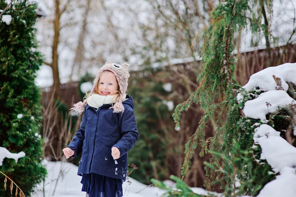 Cute happy child girl in owl hat and blue coat walking in winter snowy garden — Stock Photo, Image