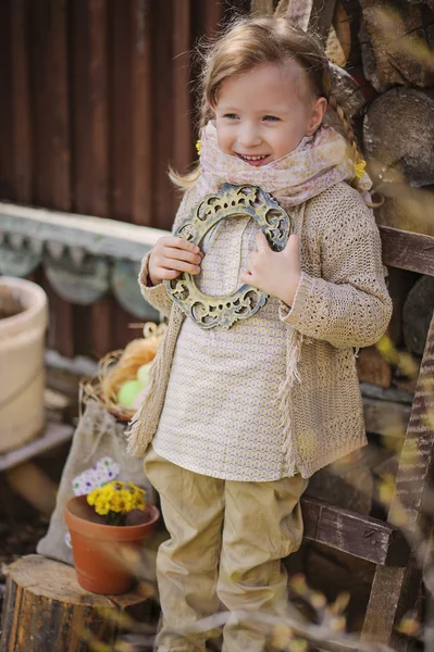 Cute happy child girl in early spring garden holding vintage frame — Stock Photo, Image