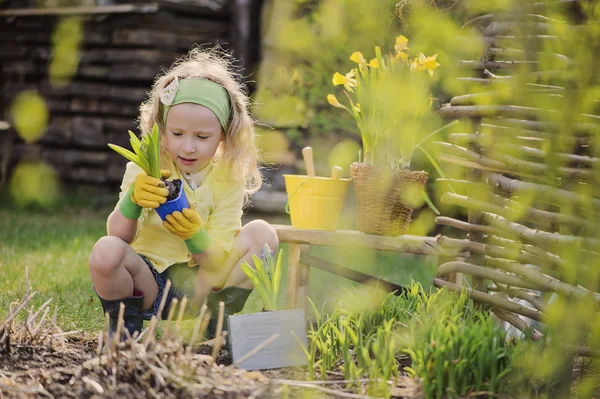 Cute happy child girl in yellow cardigan plays little gardener in spring garden