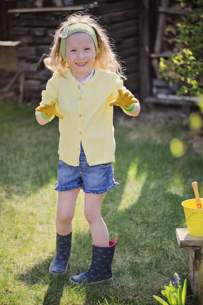 Mignon enfant fille en cardigan jaune joue petit jardinier et portant des gants de jardin dans le jardin de printemps — Photo