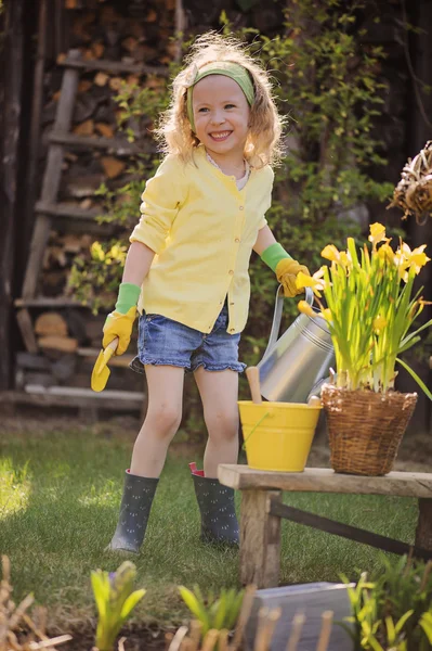 Cute blonde child girl plays little gardener and watering flowers in spring garden — Stock Photo, Image