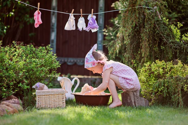 Pembe kareli elbiseli kız şirin çocuk oyuncak yıkama yaz bahçesinde çalış — Stok fotoğraf
