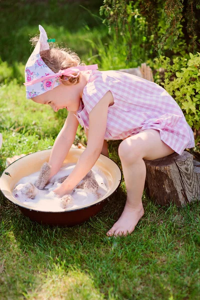 Cute child girl in pink plaid dress plays toy wash in summer garden — Stock Photo, Image