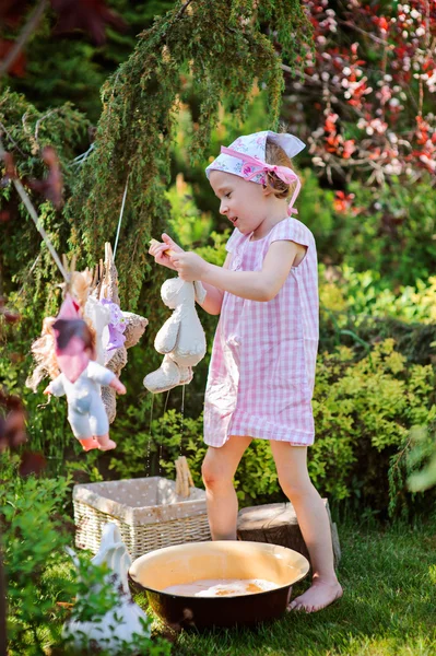 Roztomilé dítě šťastné děvče v růžové kostkované šaty a čelenka květina hrající hračka mytí v letní slunné zahradě — Stock fotografie