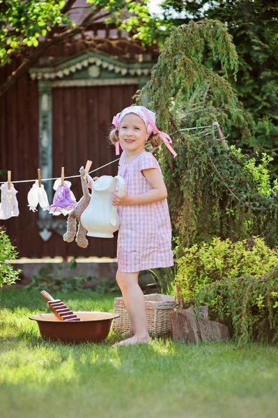 Ragazza carina felice bambino in abito plaid rosa e fascia fiore giocare giocattolo lavare in estate giardino soleggiato — Foto Stock