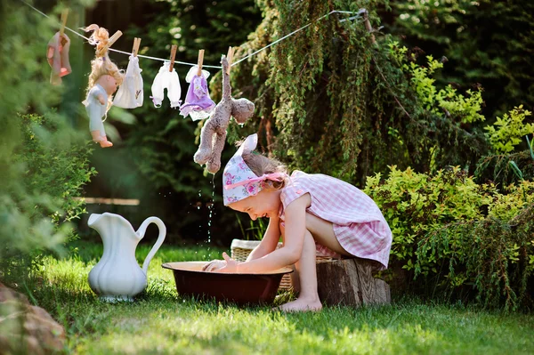 Menina criança feliz bonito em vestido xadrez rosa e flor headband jogando brinquedo lavar no verão jardim ensolarado — Fotografia de Stock