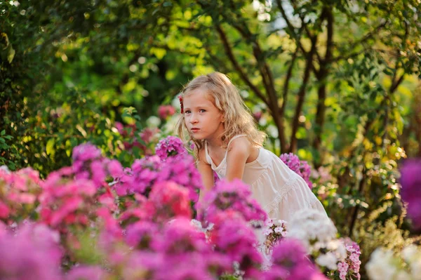 Linda niña rubia rizada que se divierte en el jardín floreciente de verano — Foto de Stock