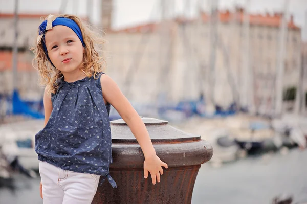 Ładny blond kręcone dziecko dziewczynka w granatowy strój chodzenie w dokach w Piran, Słowenia w letni dzień — Zdjęcie stockowe