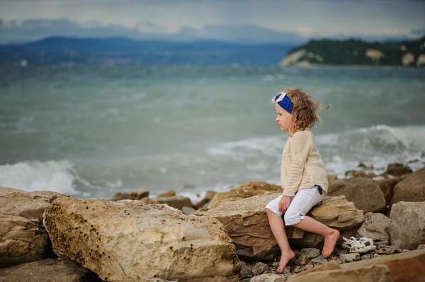 Linda niña rizada en diadema azul que se divierte en la playa de piedra en verano día ventoso — Foto de Stock