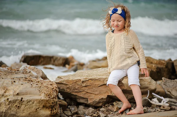 Linda niña rizada en diadema azul que se divierte en la playa de piedra en verano día ventoso — Foto de Stock