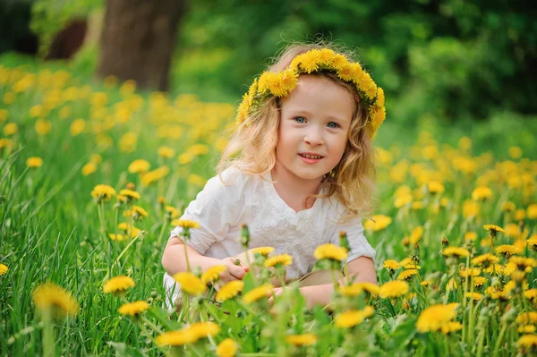 Cute happy child girl in dangelion wreath having fun on spring flower field — Stock Photo, Image