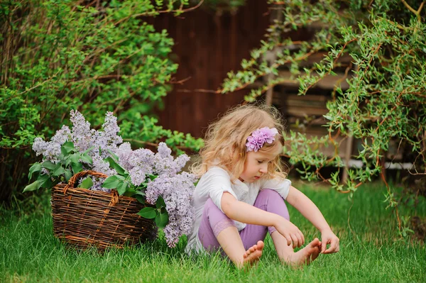 Linda niña rubia divirtiéndose en el jardín de primavera con cesta de lilas — Foto de Stock