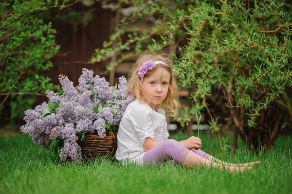 Linda niña rubia divirtiéndose en el jardín de primavera con cesta de lilas —  Fotos de Stock