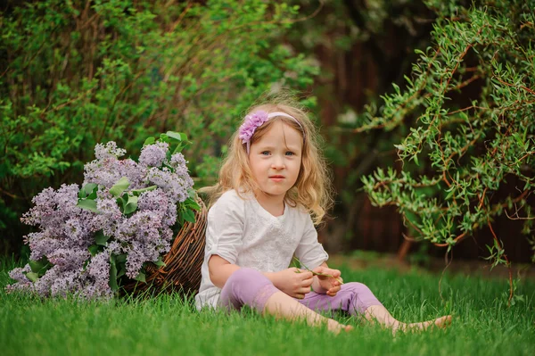 Cute blonde child girl having fun in spring garden with basket of lilacs — Stock Photo, Image