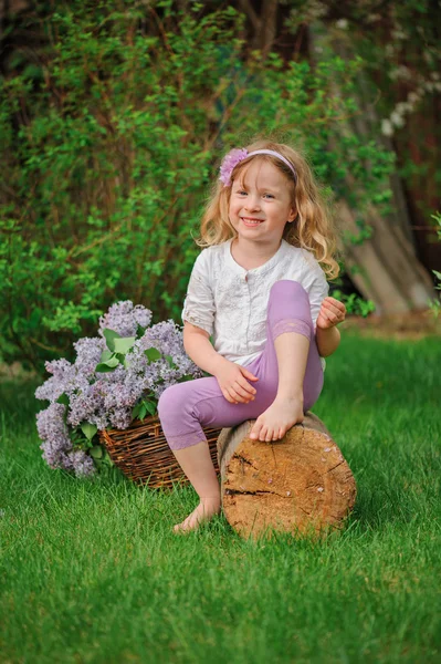 Cute blonde child girl having fun in spring garden with basket of lilacs — Stock Photo, Image