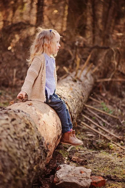 Милая счастливая блондинка девочка в трикотажном свитере и голубой рубашке прогуливаясь в раннем весеннем лесу — стоковое фото