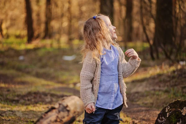 Cute happy blonde child girl in knitted sweater and blue shirt walking in early spring forest — Stock Photo, Image