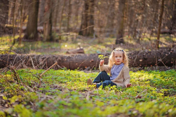 Cute blonde child girl sitting in early spring forest with green leaf — Stock Photo, Image