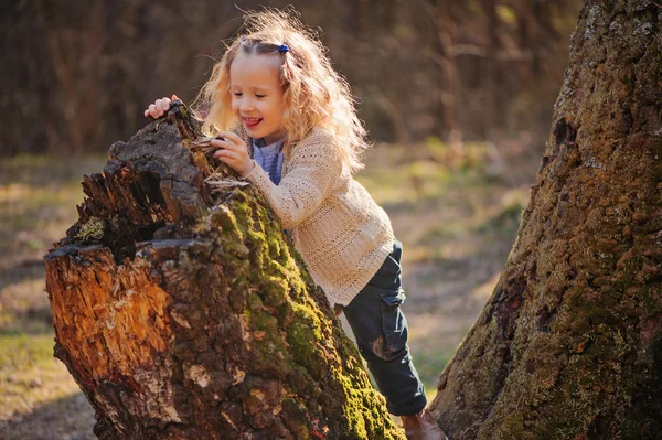Cute happy blonde child girl in knitted sweater and blue shirt walking in early spring forest — Stock Photo, Image