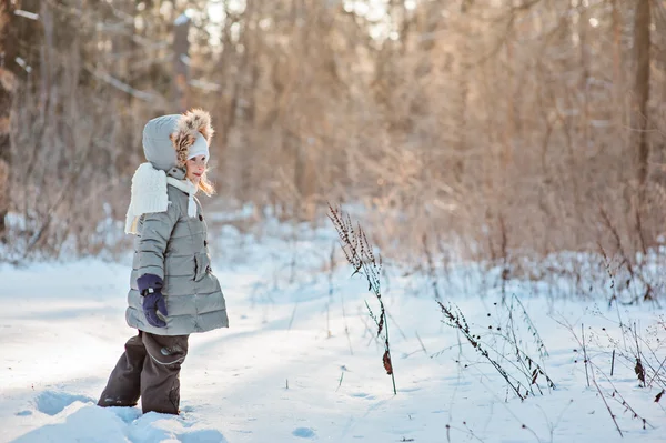 Horizontales Porträt eines schönen glücklichen Mädchens, das auf dem Spaziergang im wintersonnigen, verschneiten Wald aus der Kamera schaut — Stockfoto