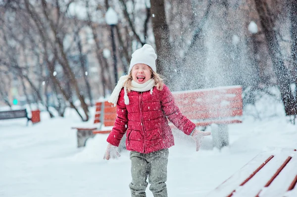 Ritratto di bambina felice in cappotto rosso che lancia neve e ride nel parco innevato invernale — Foto Stock