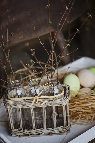 Easter eggs in nest with first spring sprigs in vintage basket on wooden table — Stock Photo, Image