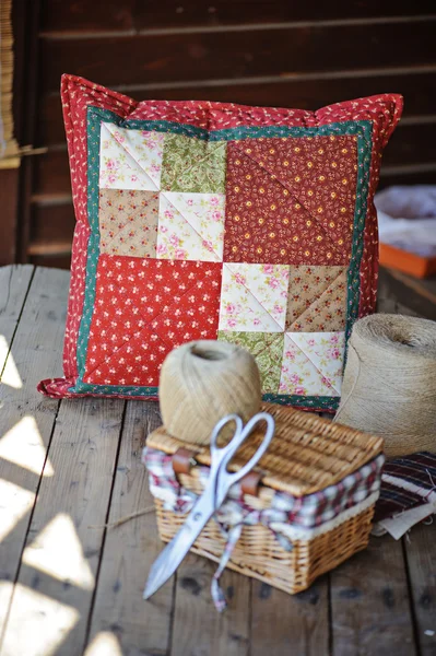 Coussin patchwork main rouge avec outils à coudre et brindilles sur table en bois — Photo