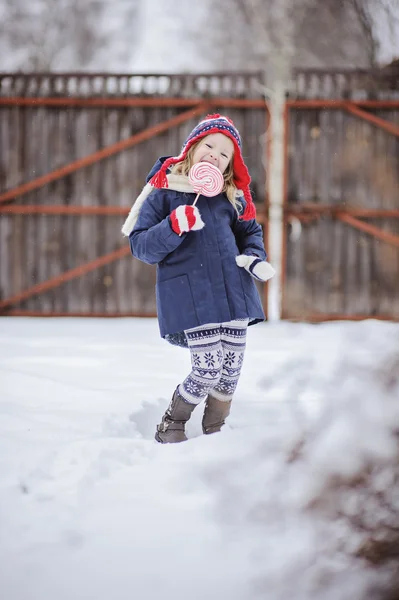 Cute child girl having fun on the walk in winter snowy garden with christmas candy — Stock Photo, Image