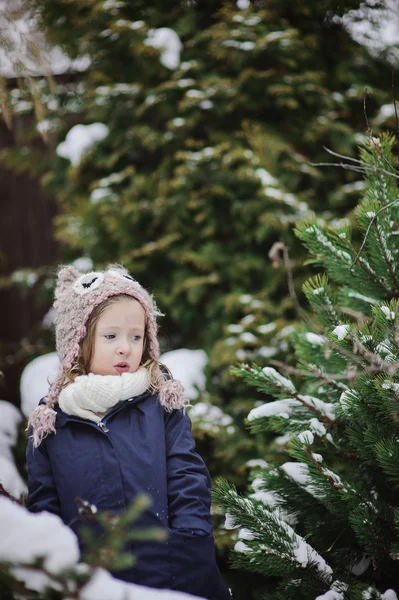 Cute child girl in owl knitted hat and blue coat on the walk in winter snowy garden — Stock Photo, Image