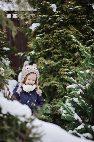Cute child girl in owl knitted hat and blue coat on the walk in winter snowy garden — Stock Photo, Image