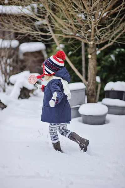 Cute child girl having fun on the walk in winter snowy garden with christmas candy — Stock Photo, Image