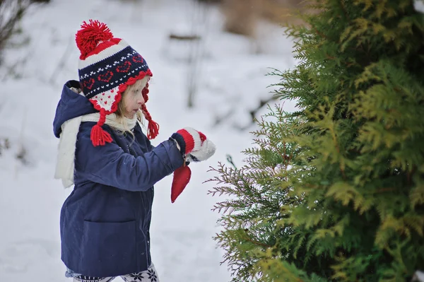 Cute child girl in christmas hat and gloves decorating tree in winter garden — Stock Photo, Image